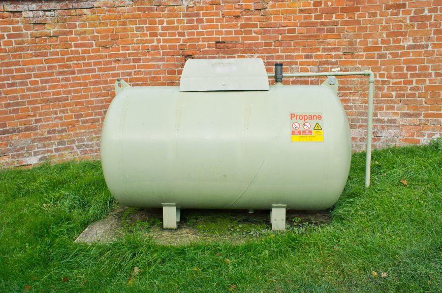 A large propane tank in front of a brick wall