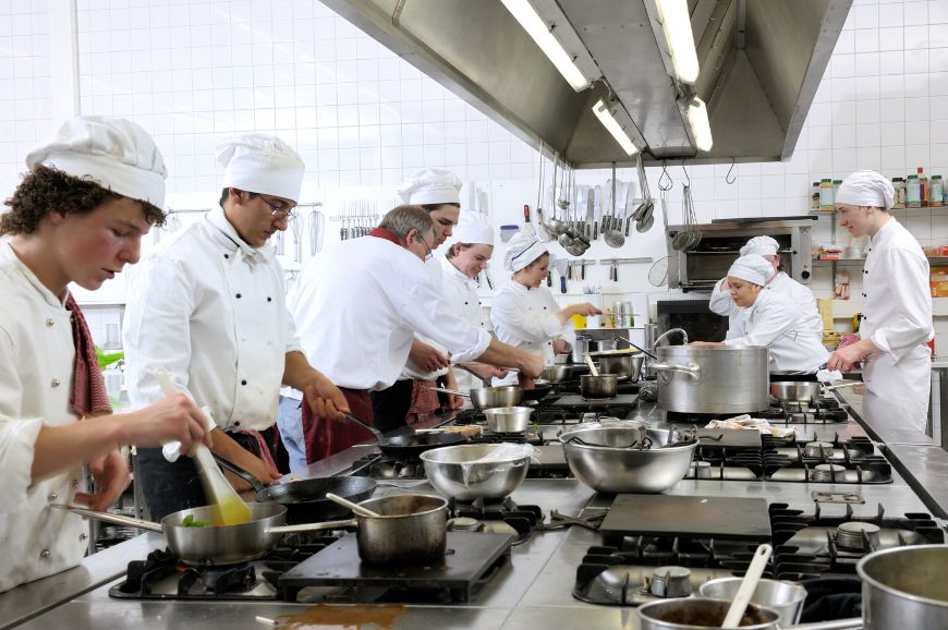 The staff of a restaurant kitchen using a propane-fueled stove top to prepare meals.