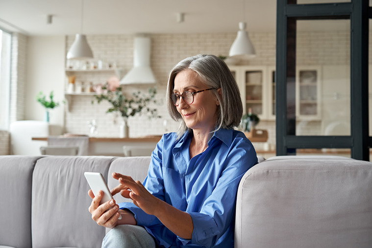 Older women sitting on couch using her cell phone to login to the customer portal